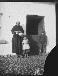 Old woman and two young boys in doorway of thatched cottage