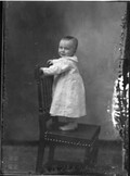 Portrait photograph of baby standing on chair n.d.