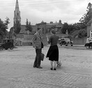 Man talking to woman in cobbled square, church visible in background, Co. Dublin