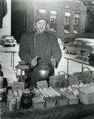 Unidentified Farmers' Market vendor warming hands. [195-?]