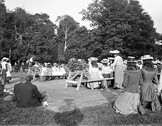 Group of children seated at tables and some kneeling, possibly a children's party or festival.