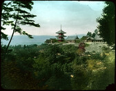 Temple and houses on hill over valley filled with trees.