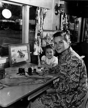 Mrs. Edith Troy painting ties in her trailer while her daughter watches.