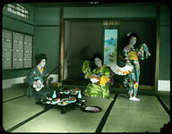 Three women with fans, musical instrument and a table set with food.