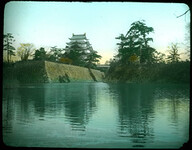 High stone embankments above river; line of trees on top of each embankments; tall building with temple roofs on one side; another building hidden behind trees on other side.