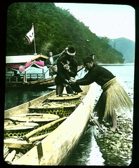 Two boats on river, a passenger boat being poled and a fishing boat filled with lidded open work baskets.