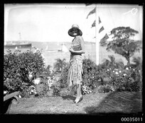 Woman with clutch bag and hat posing for the camera with a regatta in the background, 1920-1935