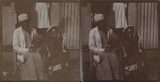 Gunbearer Muhammed bin Juma sits on a doorstep with one of his wives and a child, with Kirsti Gallen-Kallela standing in the background in October 1910.