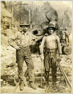 View of high rigger holding axe standing beside another employee of the Capilano Timber Company