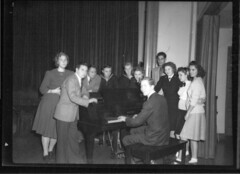 Men and women standing around grand piano n.d.