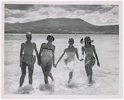 Beach scene at Oppossum Bay - four young women in water in one piece bathing costumes - view of Derwent Estuary and Mt Wellington in background