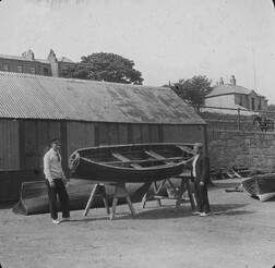 Two men pictured with rowboats in a yard - Dun Laoghaire