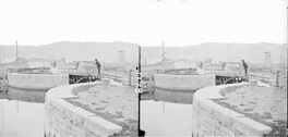 Navigation bridge (iron) on curved lock, dock on canal entrance, another bridge, towns old mill, hills, in background