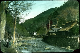 River in mountains; raised bank with houses on one side; Japanese children on side of river.