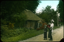 Mother and children outside rural hut with waterwheel.