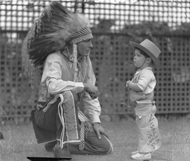 Visiting Indian Chief High Eagle talks with Johnny Schneider (aged about 3 or 4 and dressed in cowboy outfit), White City, Sydney, 11 Jan 1935 / photographer Sam Hood