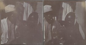 Gunbearer Muhammed bin Juma sits on a doorstep with one of his wives and a child in October 1910.