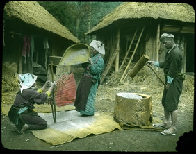 Two women winnowing rice and man pounding rice flour.