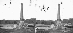 Square obelisk by footbridge with iron railing over wide stream, woods in background, Drogheda