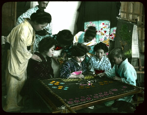 Group of women and one man watching young woman working on large embroidery.