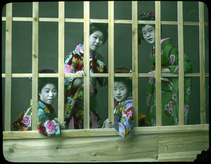 Four women smiling and leaning through openings in lattice work.